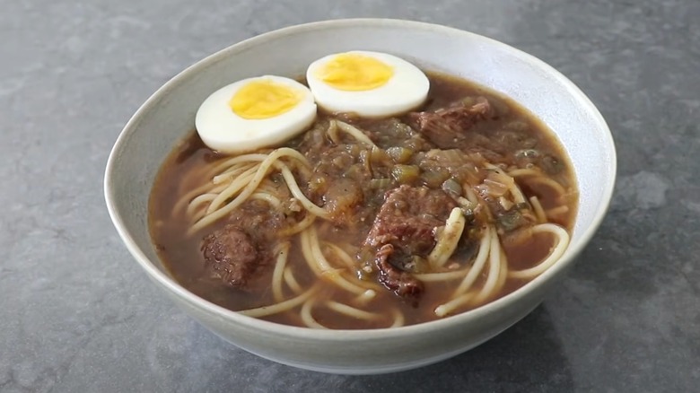 A bowl of yakamein noodle soup with a sliced boiled egg