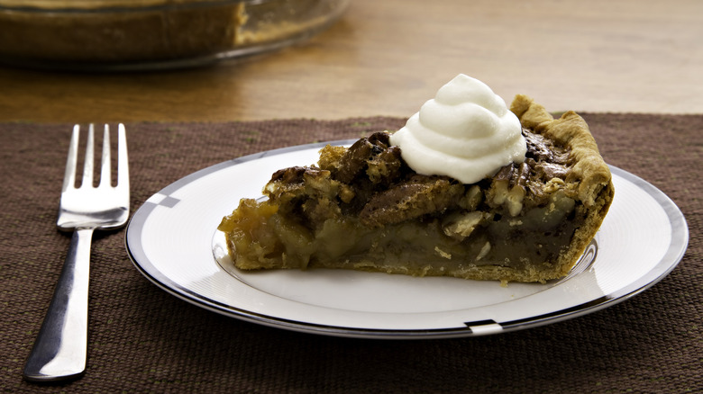 Slice of pecan pie with whipped cream and fork