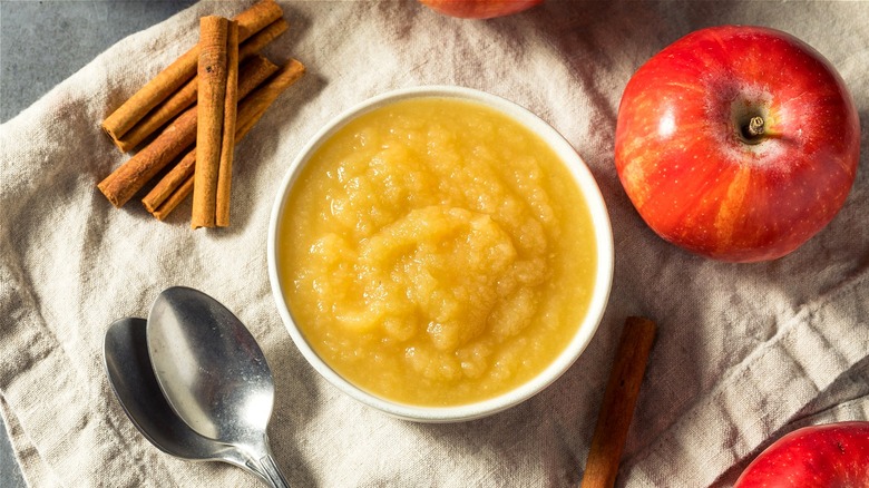 Applesauce in white bowl with spoon next to whole apple