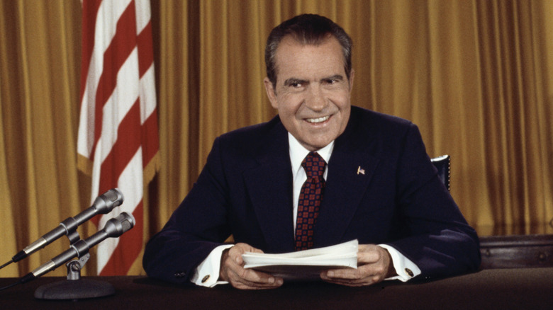 Richard Nixon seated at a desk holding papers