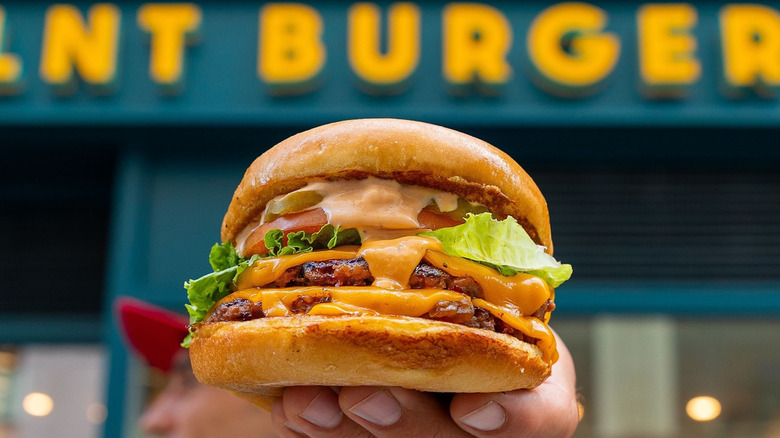 Hand holds burger up in front of PLNT Burger restaurant