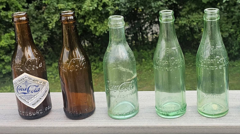A row of various straight-sided Coca-Cola bottles