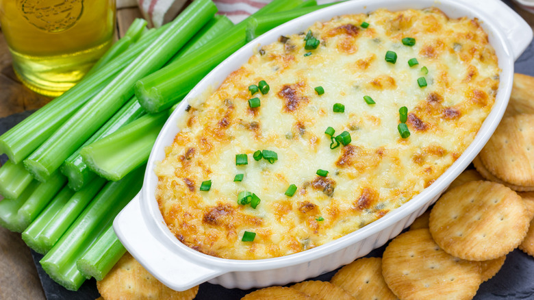 Baked crab dip in a ceramic dish, with celery sticks and crackers