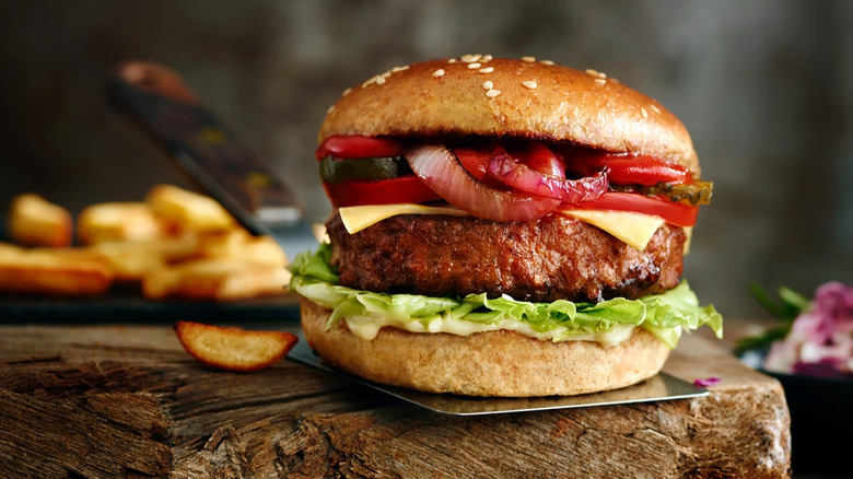 A hearty beef burger placed on a spatula over a wooden board