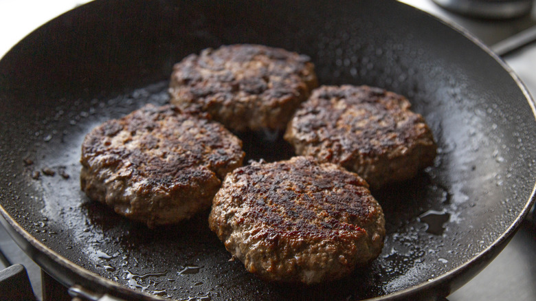 Four burger patties stuffed with oysters in a skillet
