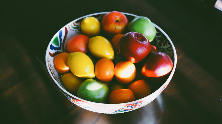 Sun shining on a bowl of imitation fruit on a dark table