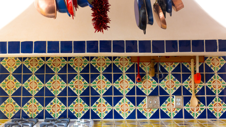 A kitchen backsplash of colorful Mexican tile with pots and pans hanging overhead