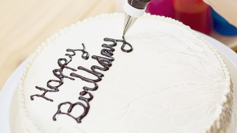 Piping "happy birthday" onto a frosted cake