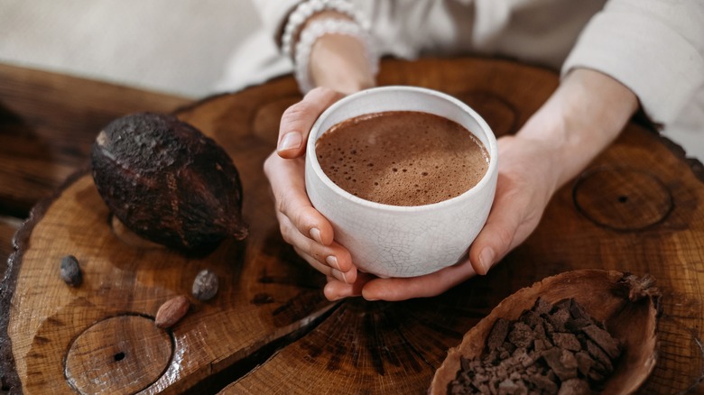 hands holding hot chocolate above wooden platter