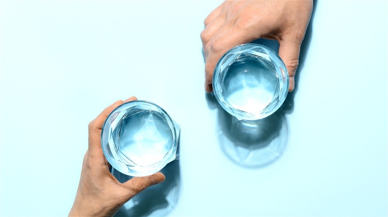 Two hands holding water glasses