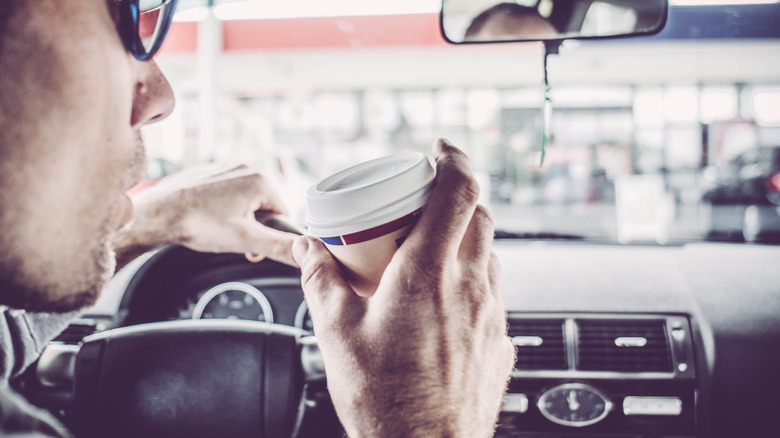 A man in a car, drinking coffee at a gas station