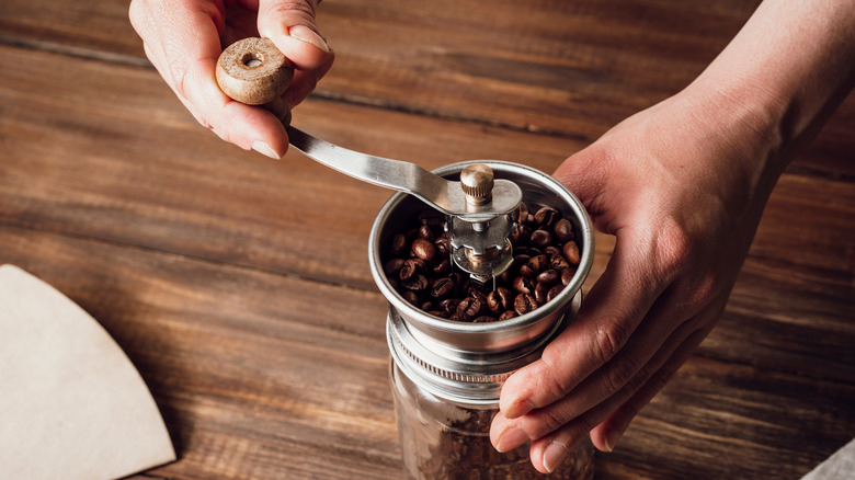 person's hands grinding beans manually on wood table