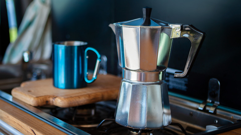 Steel Bialetti pot on stove blue coffee cup on wooden board