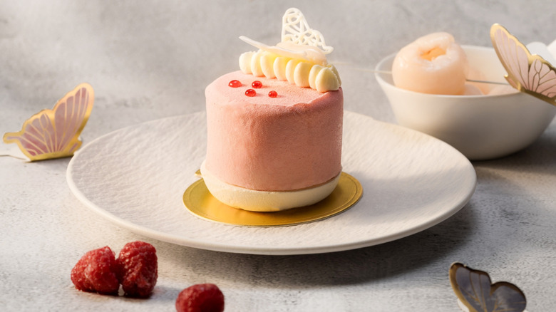 A lychee raspberry mousse artfully placed on a golden circle on a white plate