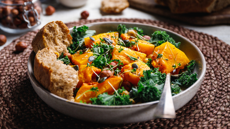A plate full of fall salad with bread and a fork on a woven placemat