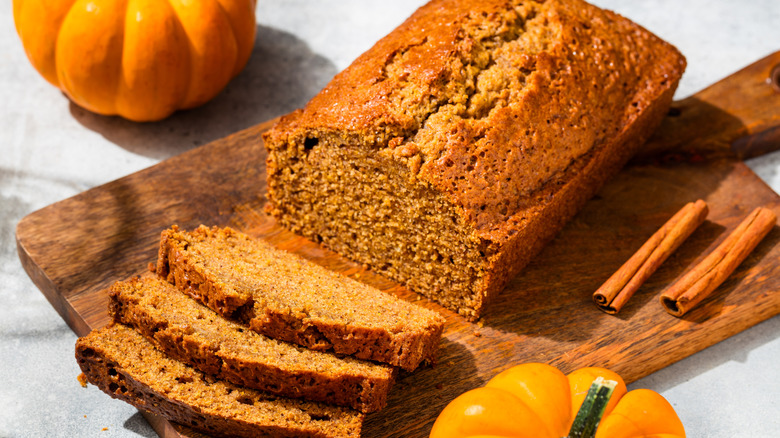A loaf of pumpkin bread and a few cut slices on a wooden chopping board