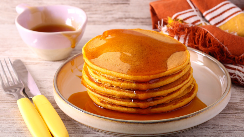 A stack of pumpkin pancakes topped with syrup on a plate