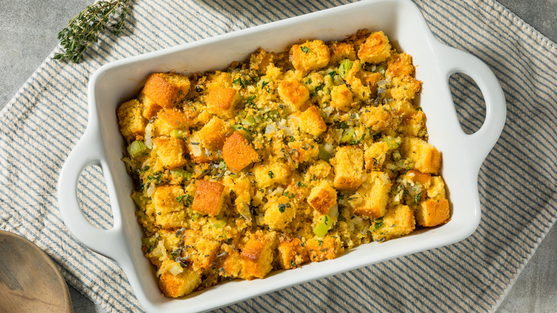 A white baking dish full of herby orange stuffing on a striped cloth