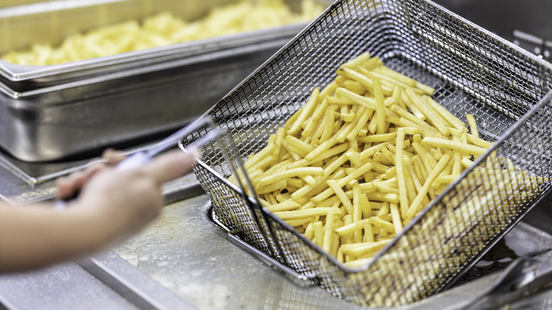 Hand holding a frying pan with french fries at a commercial kitchen.