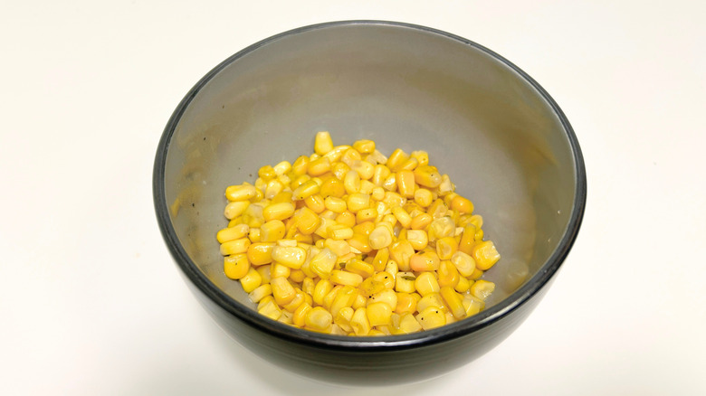 A black bowl of Texas Roadhouse buttered corn against a white background