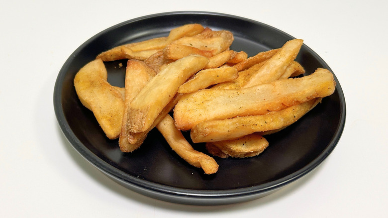 A black plate of Texas Roadhouse steak fries against a white background