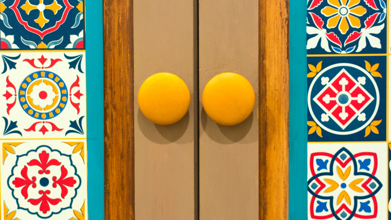 Round yellow cabinet pulls on wooden doors with multicolor patterned tiles