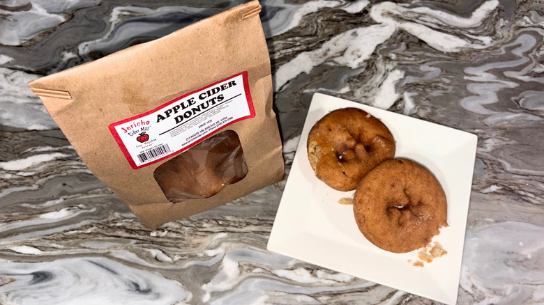 A brown paper bag of donuts next to a plate with two donuts against a countertop