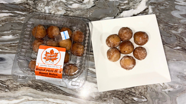 A package of donut holes next to a plate of seven donuts against a countertop