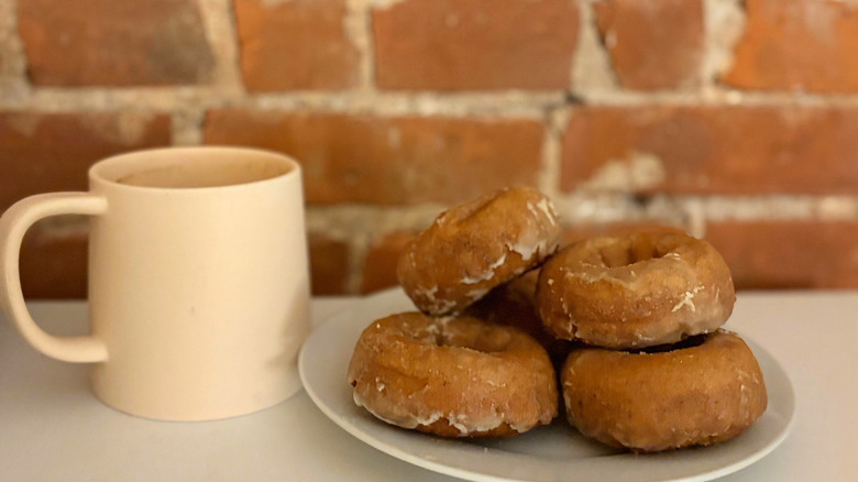 A coffee cup next to a plate with a pile of apple cider donuts