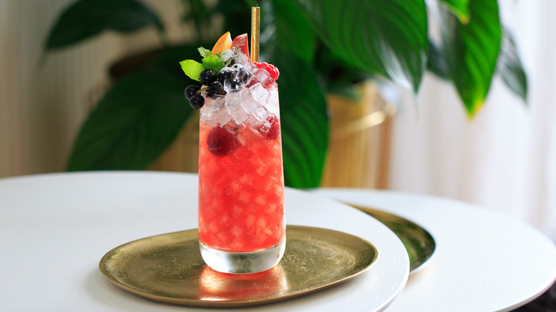 Red cocktail garnished with berries and mint