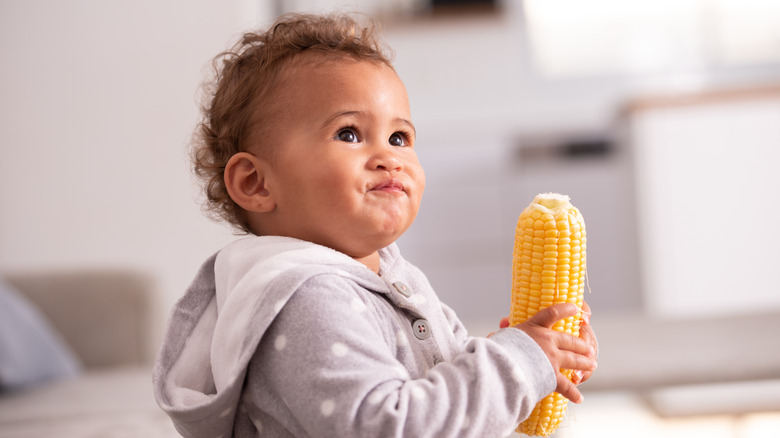 Small baby eating corn on cob