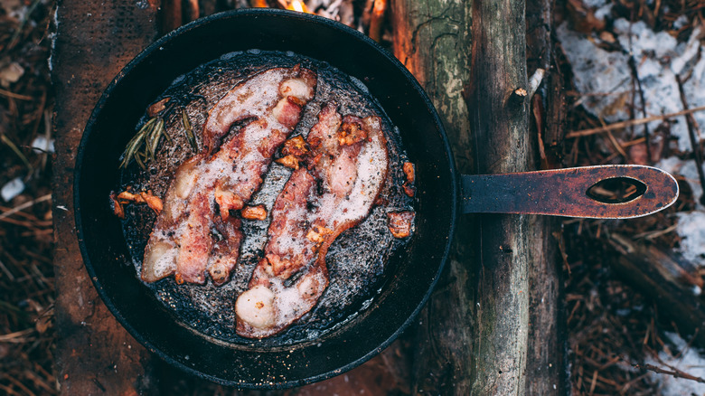 bacon cooking in skillet over fire