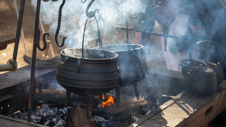 Historic cast iron pots suspended outdoors over smoldering embers