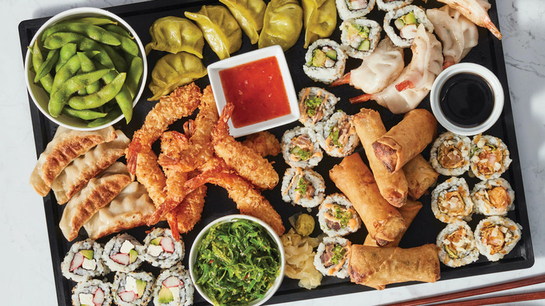 A platter of Wegmans sushi with edamame, gyoza, spring rolls, California rolls and sauces
