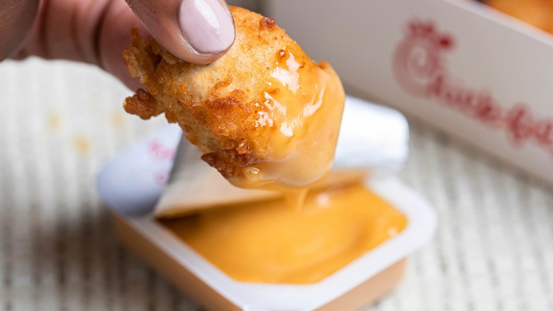 Person dipping Chick-fil-A nugget into orange sauce