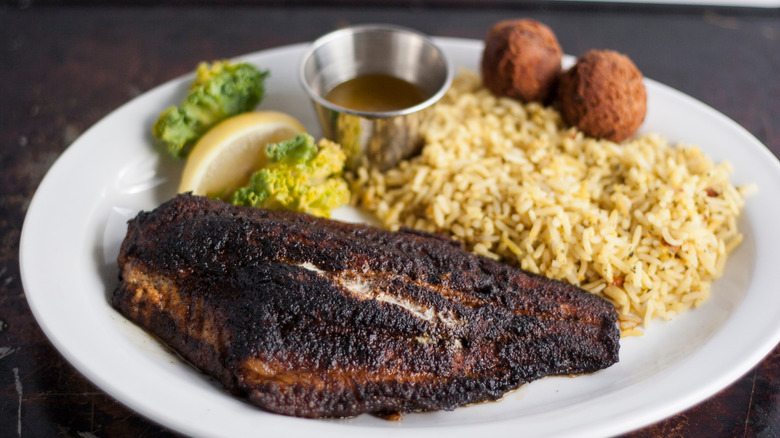 Blackened catfish on a plate with rice and hush puppies