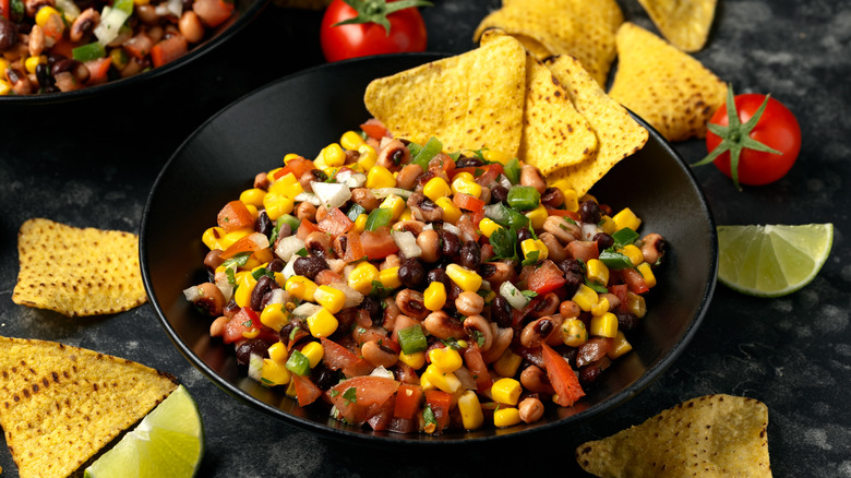 A bowl of cowboy caviar dip with beans, corn, diced tomatoes & peppers, cilantro, and tortilla chips