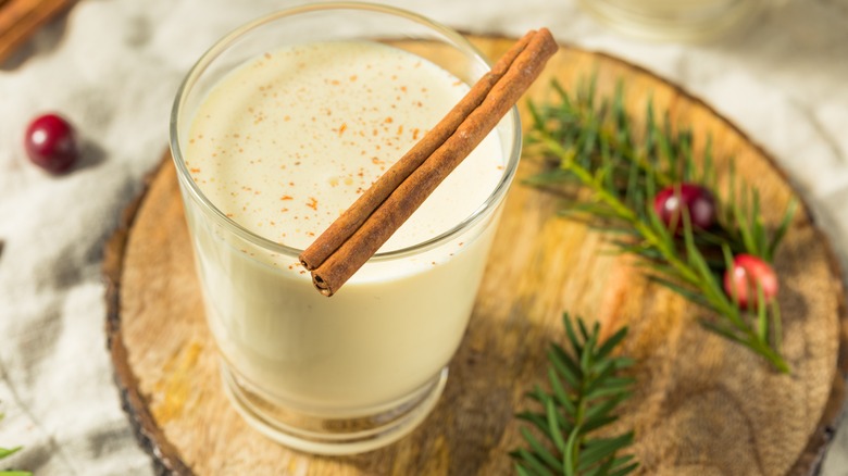 Cup of eggnog on a wooden board with rosemary and cranberries next to it