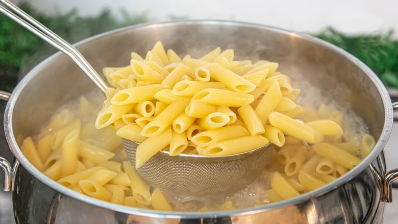 Spooning penne pasta out of boiling water