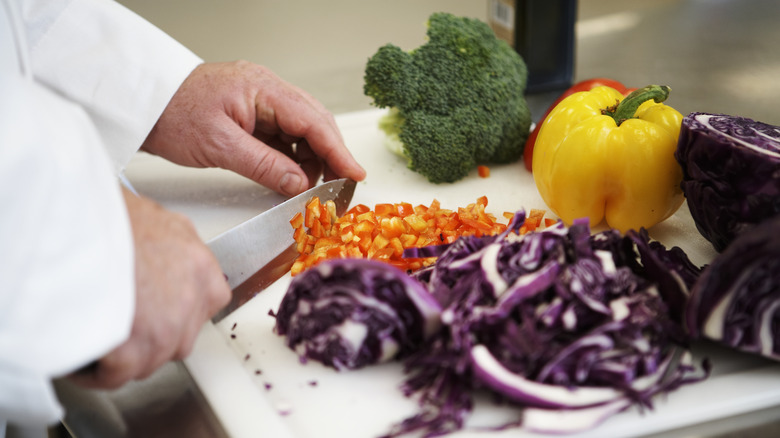 A cook chops up a red bell pepper near red cabbage