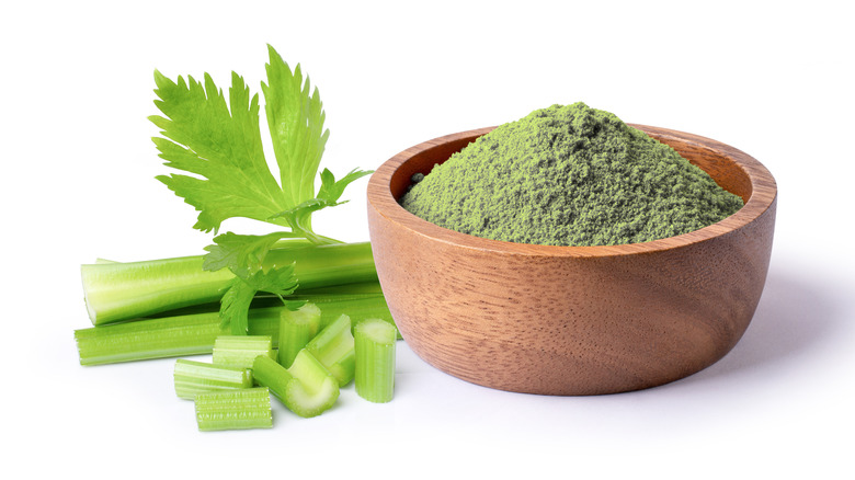 Celery powder in a wooden bowl next to fresh celery stalks