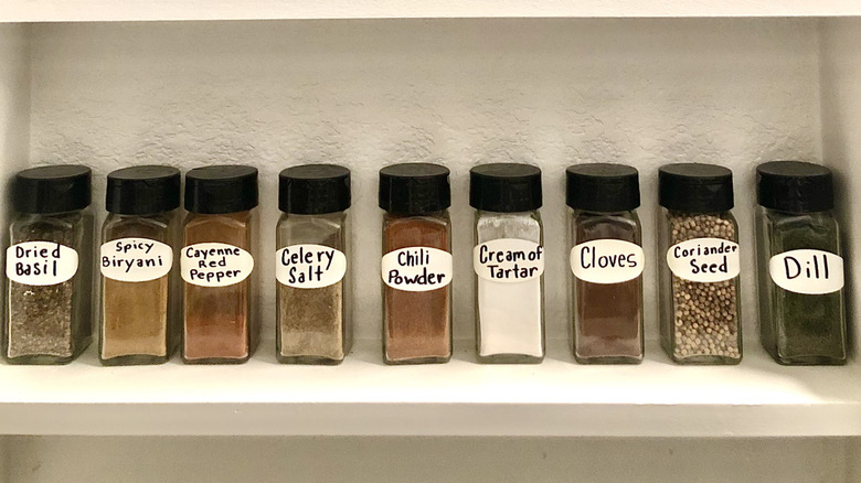 A line of spices in glass jars on a cabinet shelf with homemade labels