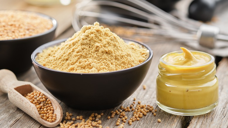 brown mustard powder, mustard, and mustard seed on wooden table