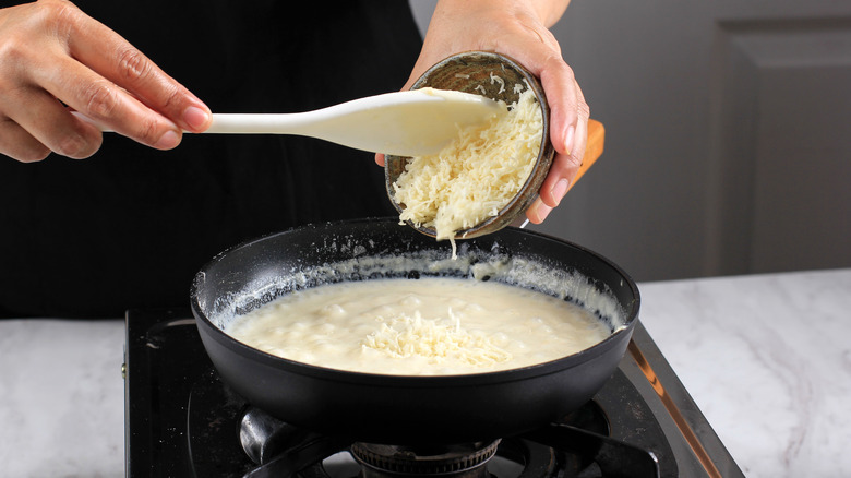 woman adding cheese to bechamel sauce