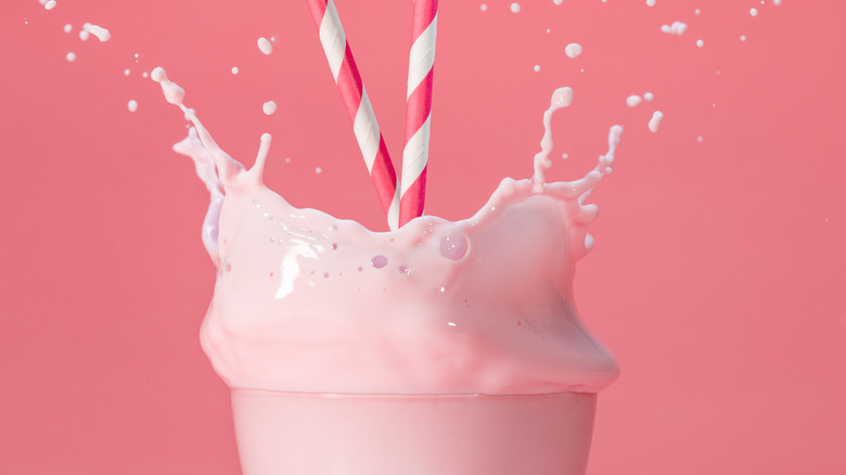 Glass of strawberry milk splashing out of glass with two straws