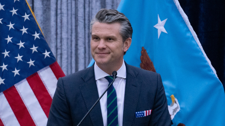 U.S. Secretary of War Pete Hegseth smiling from podium.