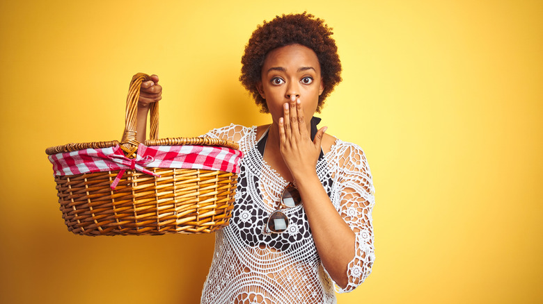 Woman holding a picnic basket with her hand over her mouth in awe