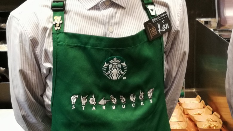 Starbucks barista in green apron with embroidered sign language