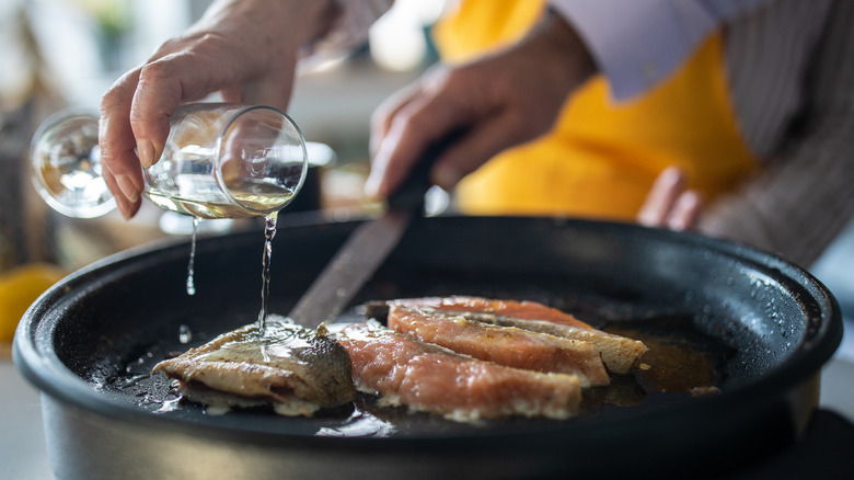 Pouring white wine into pan of fish filets