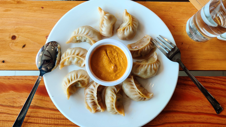 Momo around cup of sauce on a plate